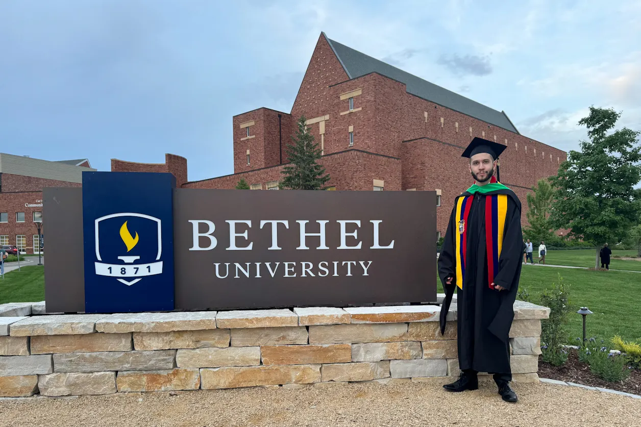 Ivan Nunez GS'24 stands in front of Benson Great Hall celebrating his graduation.