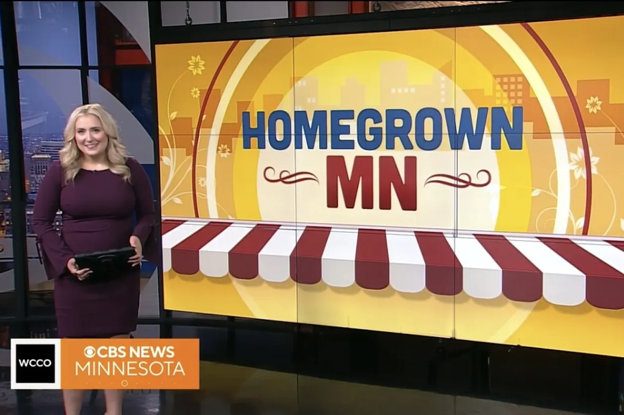 Beret Leone stands next to a screen that says Homegrown MN. She is anchoring at the WCCO station and is wearing a purple dress.