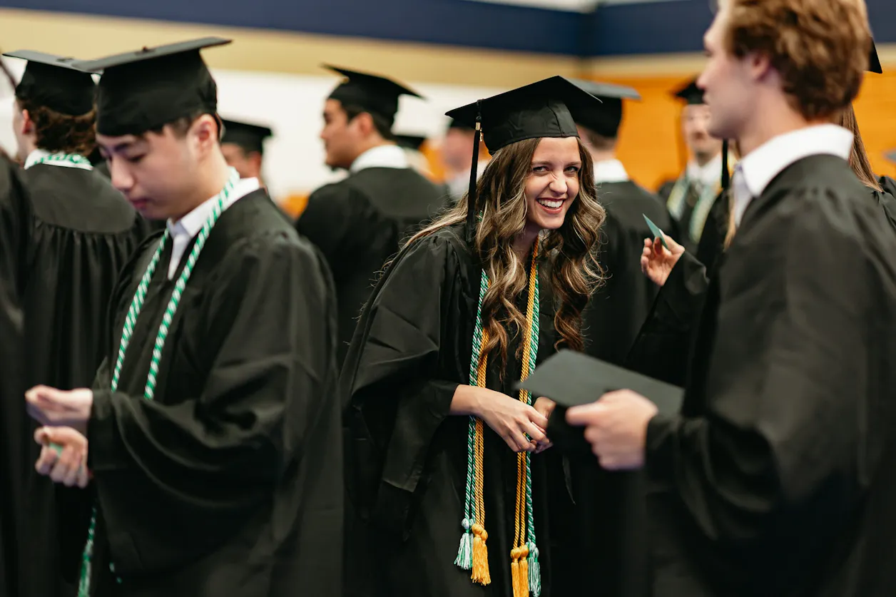 A smiling Bethel University graduate in cap and gown celebrates with classmates at commencement.