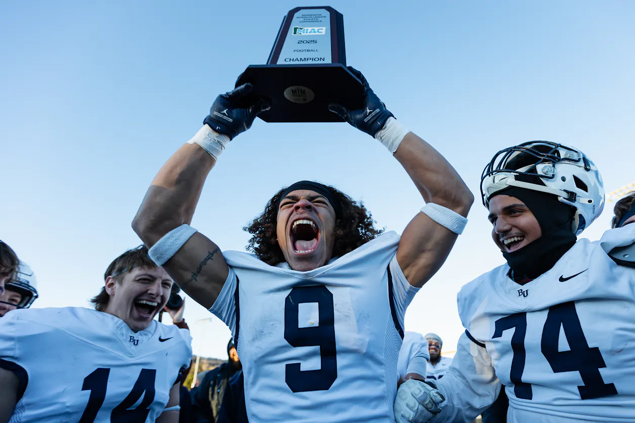 A football player holds up the MIAC Championship 2025 trophy. 