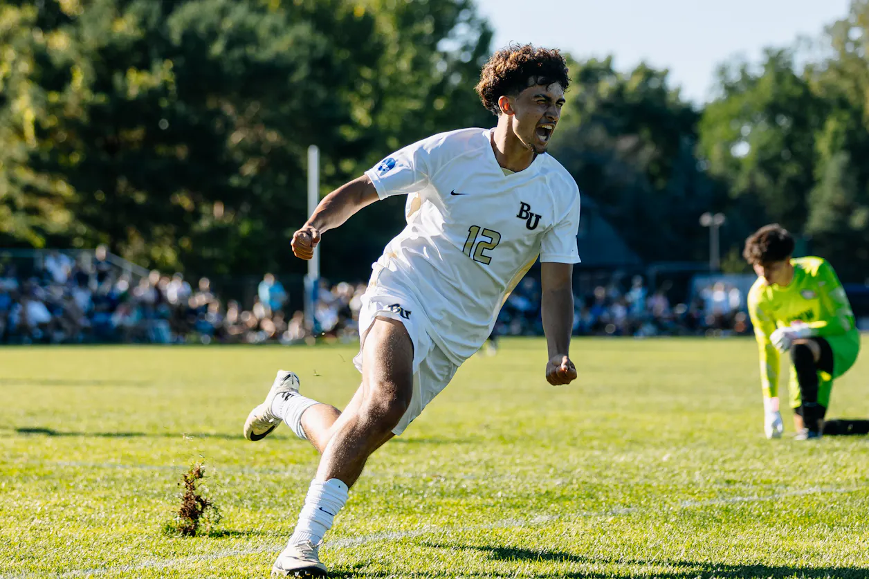 A Bethel male soccer player wearing a white jersey celebrates after a successful play.