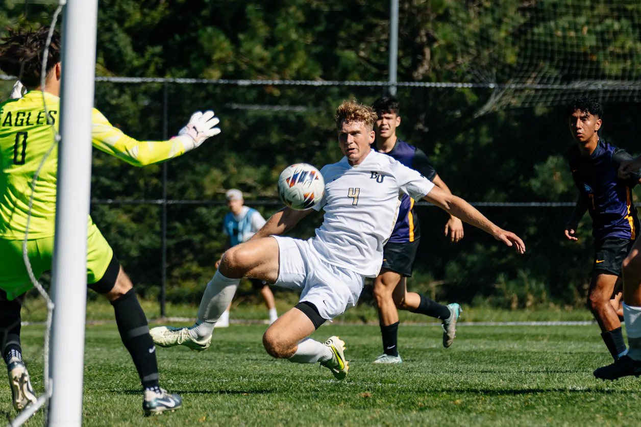 A goalie wearing bright yellow attempts to block a goal against a Bethel soccer player.