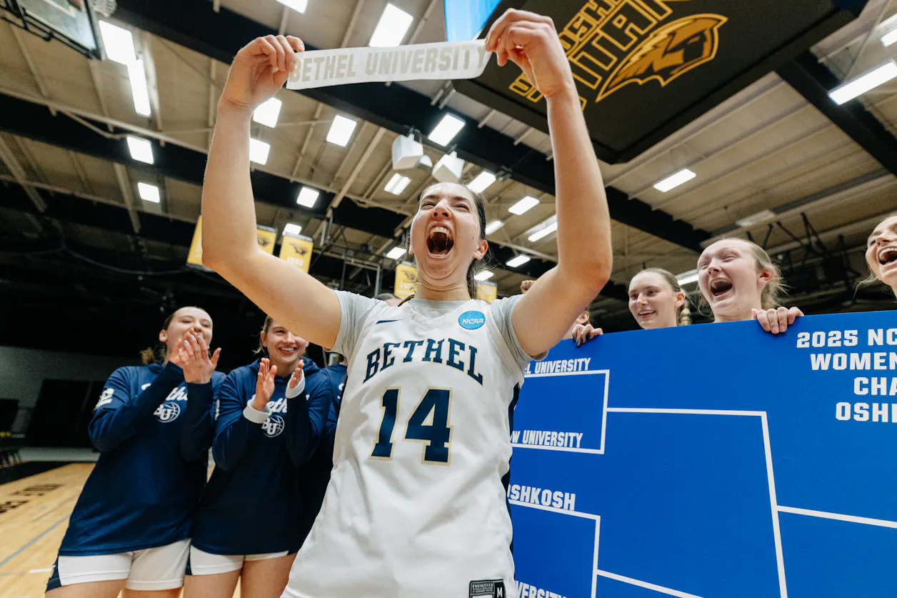 A women's basketball player celebrates a significant win in playoffs by holding up a Bethel University pennant. 