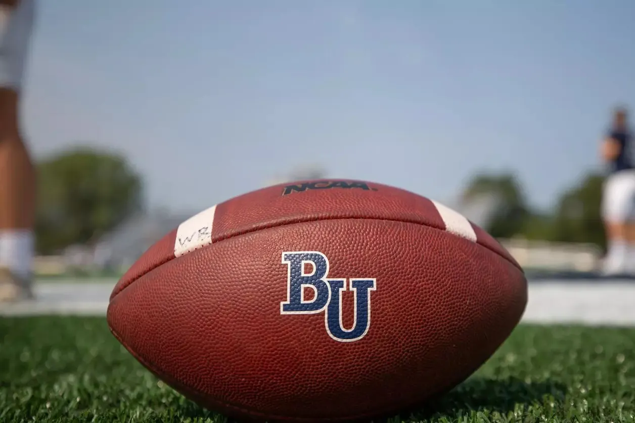 Bethel football on field, with players blurred in background.