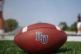 Bethel football on field, with players blurred in background.