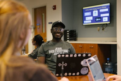 Smiling student in a “Jesus Over Everything” shirt works on a laptop during a career prep session.
