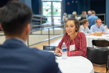 Student in red striped shirt speaks with a peer during a roundtable event at a BethelBiz event.