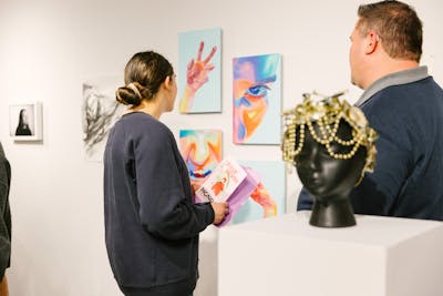 Visitors viewing vibrant paintings at an art show. 