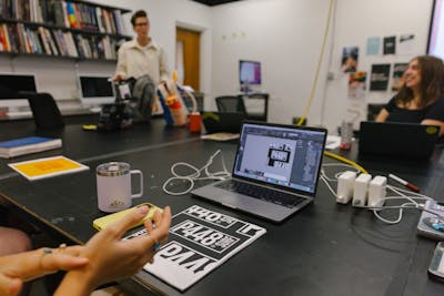 Lively classroom with students and professor discussing graphic design projects.