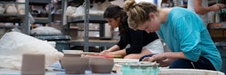 Art students sitting at throwing wheel in ceramics studio