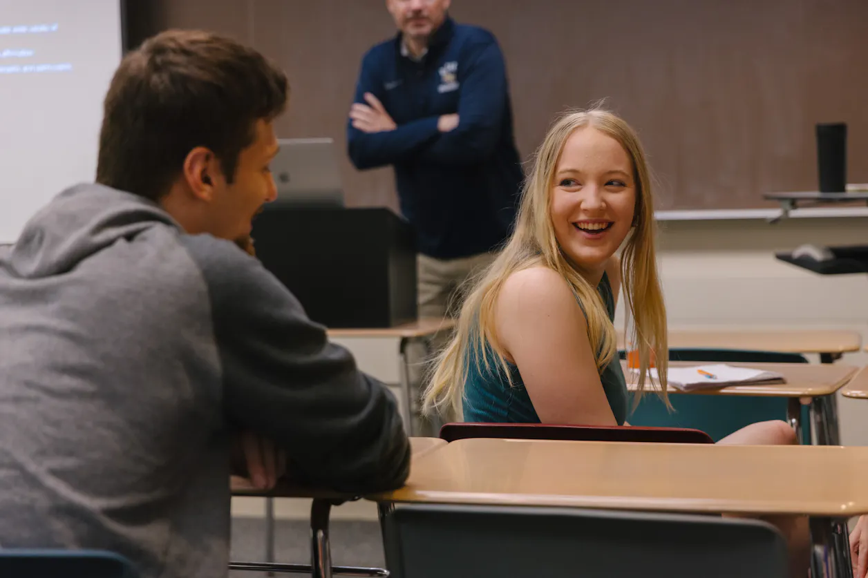 Student in green tank top smiles back at peer. 