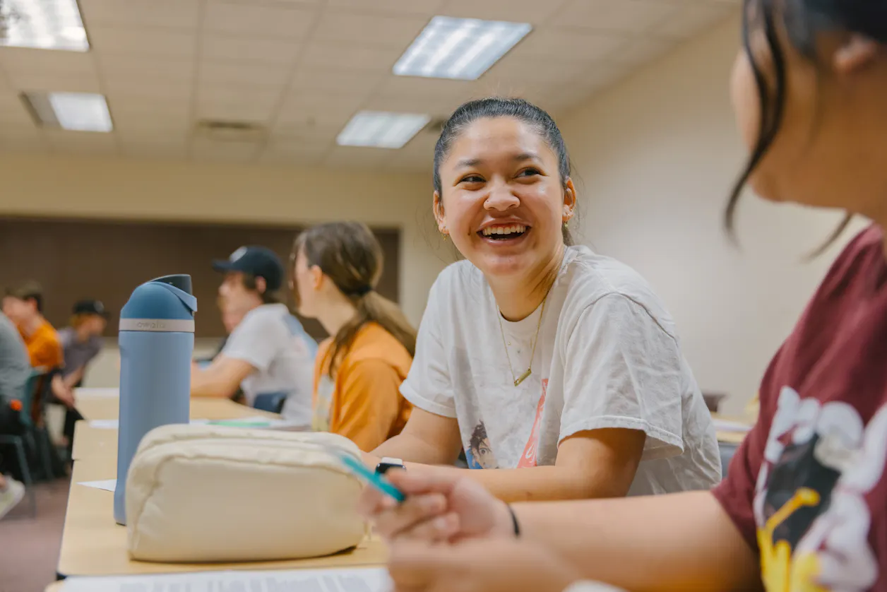 Student in white T-shirt smiles at peer. 