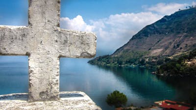 A serene view of a lake with a cross in the foreground, symbolizing faith and reflection.