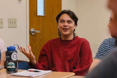 A Bethel University student actively participating in a classroom discussion, gesturing with enthusiasm while speaking.