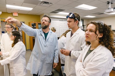 A professor points to a board while explaining an experiment to engaged students.