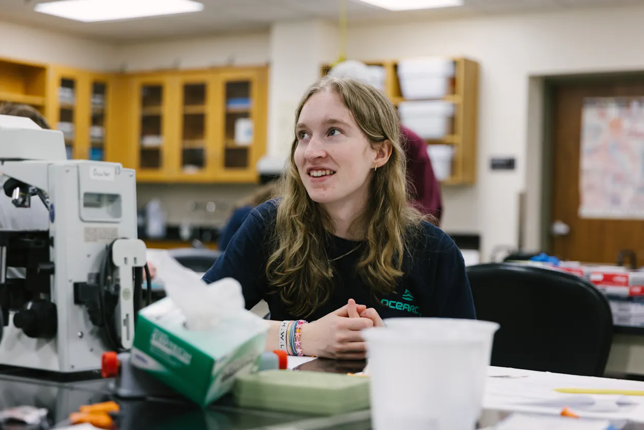 A student in a lab coat listens attentively in a classroom.