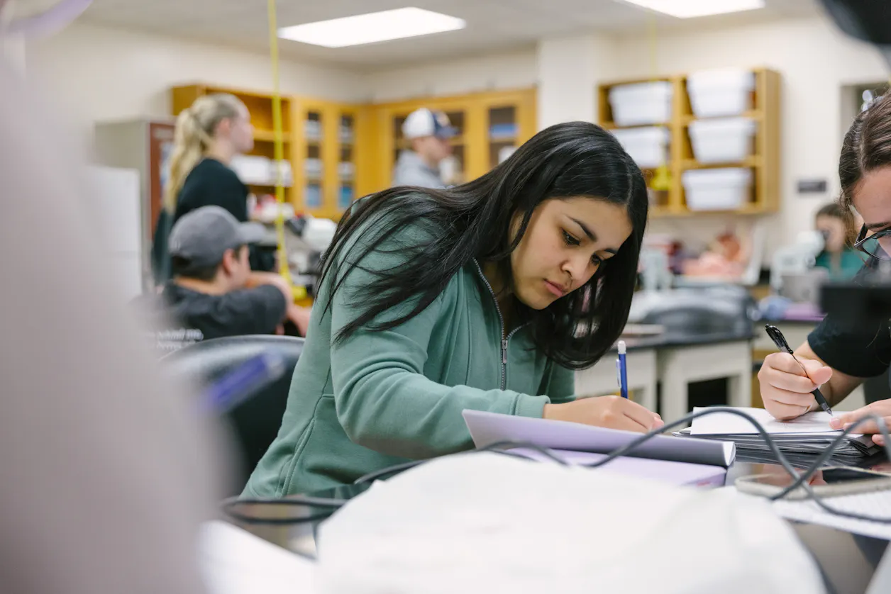 A student focuses on writing notes during a biology lab session.