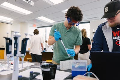 A student uses a pipette in a busy lab environment.