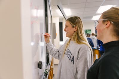 Student writing equations on a whiteboard in a lab. 