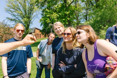 A group of students is intently observing a professor holding a small bird during an outdoor class.