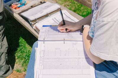 A student is meticulously recording data in a binder while outdoors.