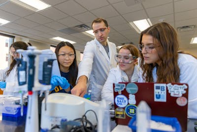 Group of students and a professor in lab coats, discussing an experiment.