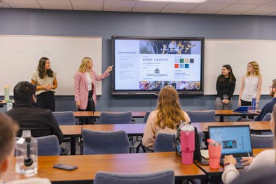 Group of students presenting a project in front of a screen displaying their work.