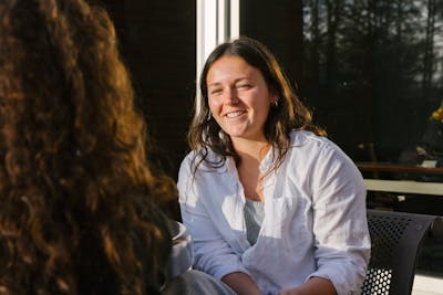 A student smiling while talking to another student outside.