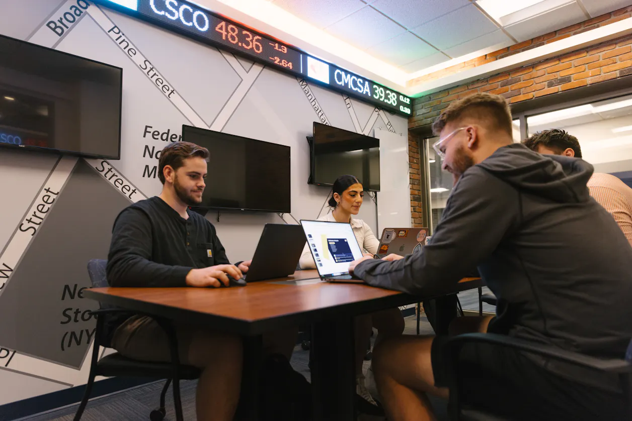 Students working in a business lab, focusing on their laptops.