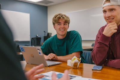 Bethel University students having a discussion around a table, with laptops and notebooks in front of them.