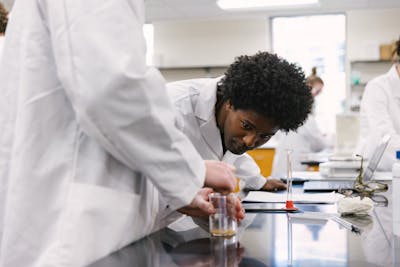 A student in a lab coat leans over a beaker, focusing on a chemical experiment.