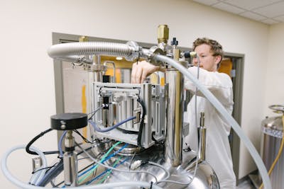 A student works with high-tech lab equipment, focusing on adjusting settings.