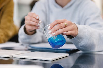 A close-up of a student stirring a blue liquid in a beaker during a chemistry experiment.