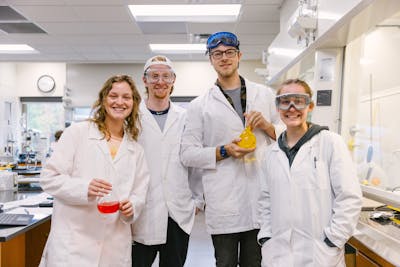 Group of students posing with lab equipment in a chemistry lab.