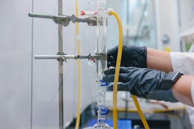 Close-up of gloved hands adjusting a glass apparatus in a chemistry lab.