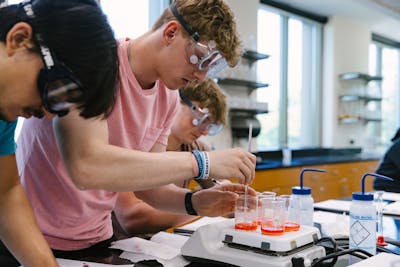 Students in safety goggles conducting a chemistry experiment with beakers.