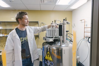 Student in lab coat operating a large, shiny lab apparatus.