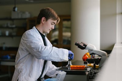 Student in a white lab coat performing a chemistry experiment with lab equipment. 