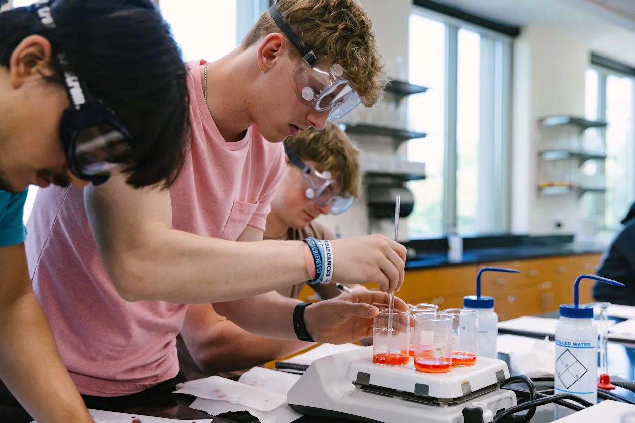 A group of Bethel University students conducting an experiment in a chemistry lab, carefully measuring liquids into test tubes.