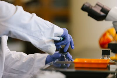 Close-up of a student's hands in blue gloves, handling lab equipment carefully.