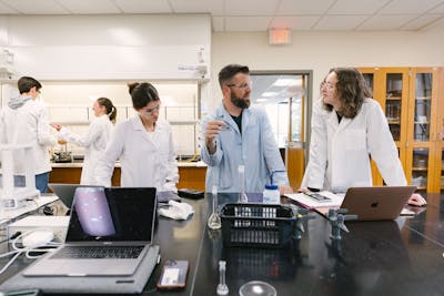 Students in lab coats and professor, engaged in a discussion about their experiment.