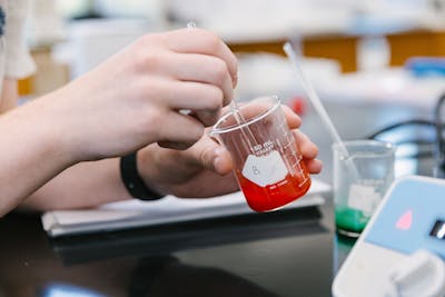 Student stirring a red liquid in a beaker during a lab experiment.