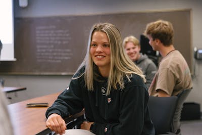 Student smiles while seated in a classroom, engaging with the group. 