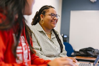 A student seated with a laptop in front of her engages in classroom activities.