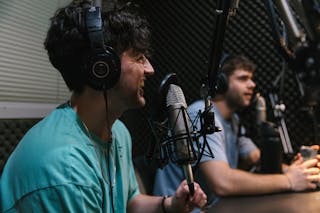 Two students in a podcast studio, one speaking into the microphone and the other listening. 