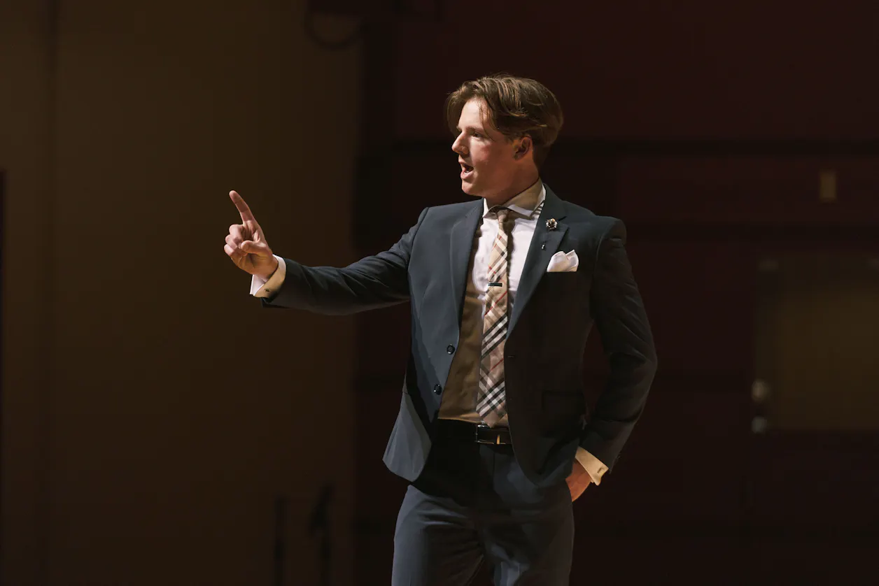 A Bethel University student delivering a passionate speech on stage, dressed in a formal suit. 