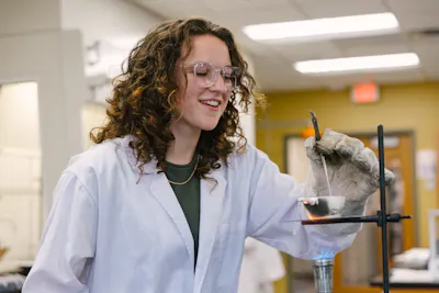 Student smiles while heating a sample over a lab burner.