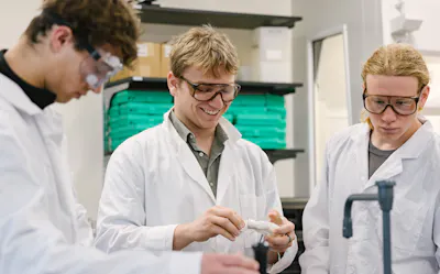 Students in lab coats examine a specimen during a hands-on science activity.