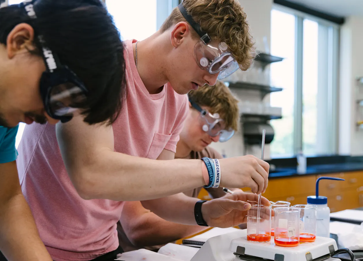 Students wearing safety goggles mix solutions during a laboratory experiment.