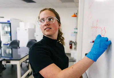 Student draws a molecular structure on a whiteboard in the lab.